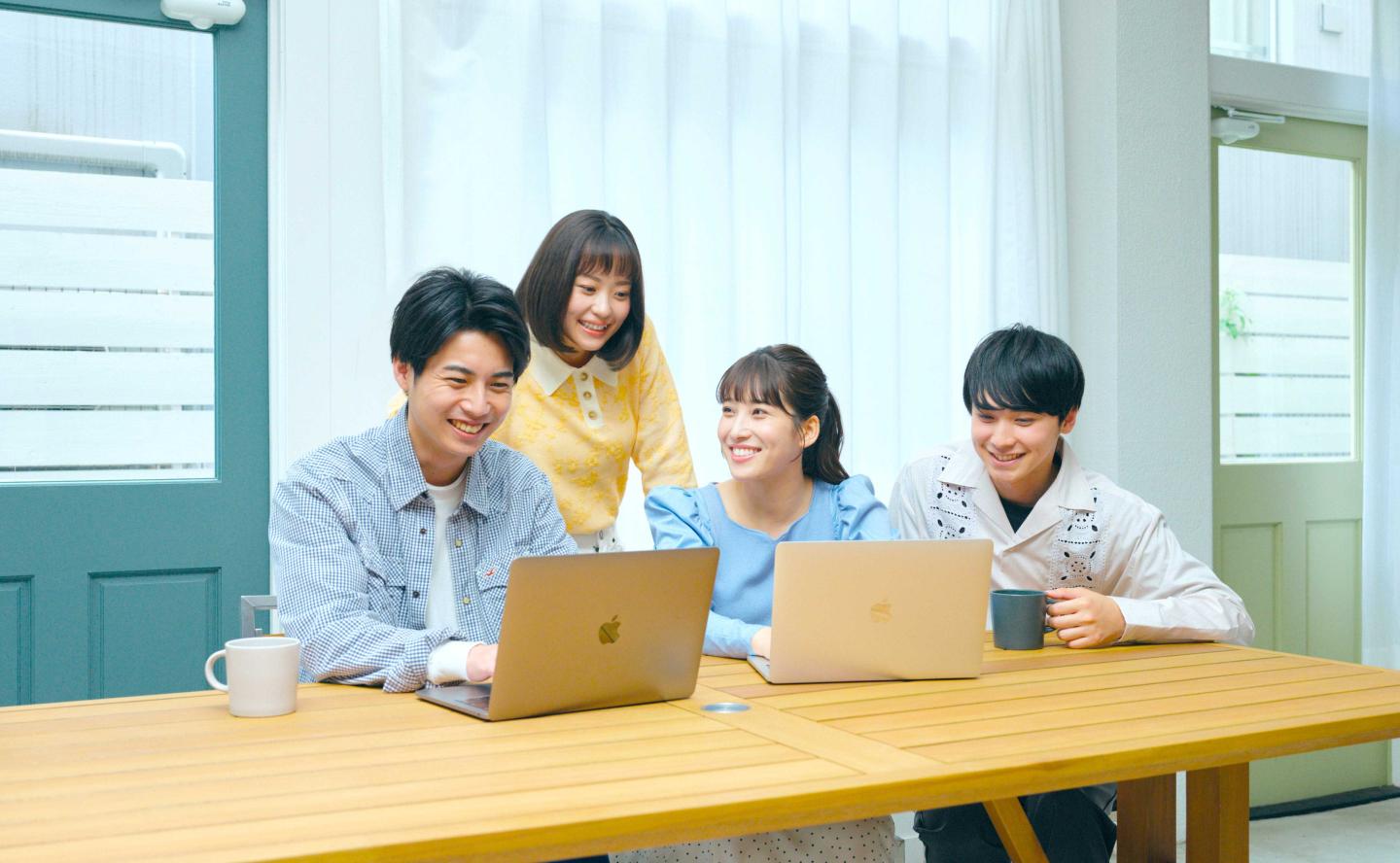 Four young people smiling while using laptops at a table