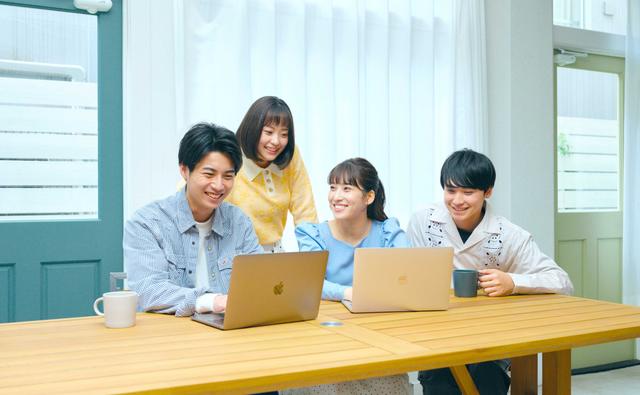 Four young people smiling while using laptops at a table